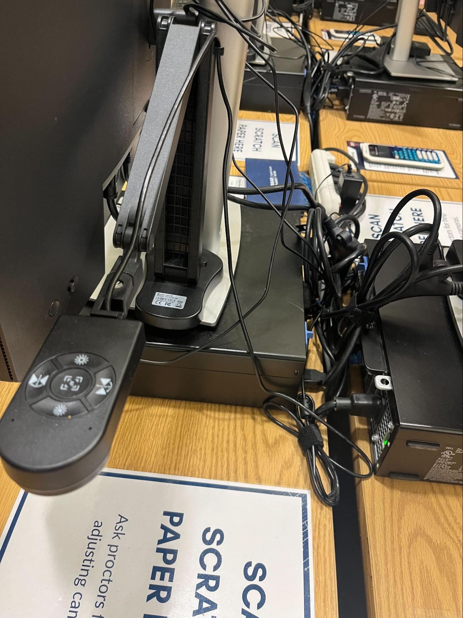 The document camera's folding arm and control head mounted alongside a monitor base, with USB and power cables routed behind
